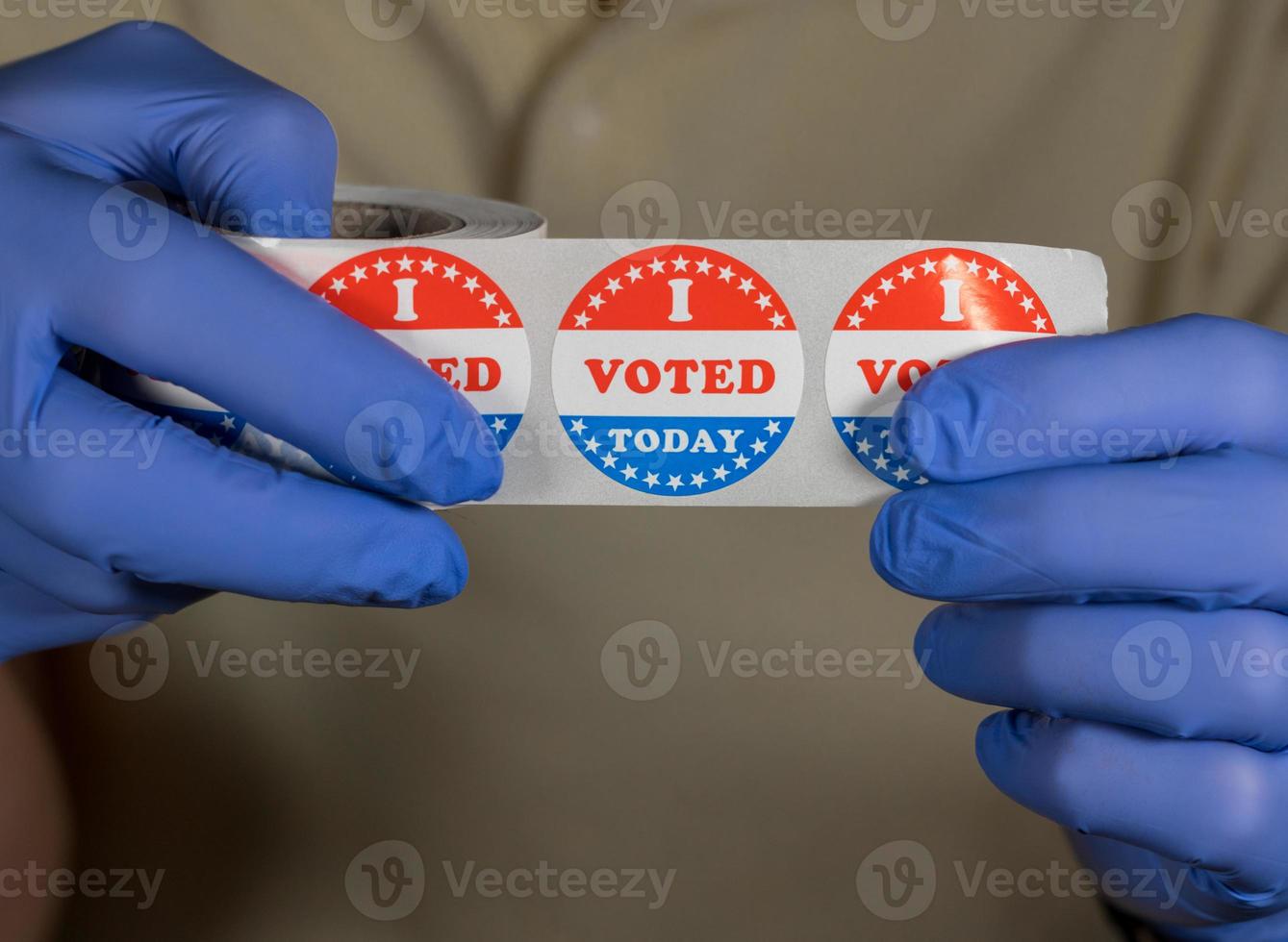 Gloved hands holding roll of I Voted Today stickers or buttons ready for voter who voted in person in election photo