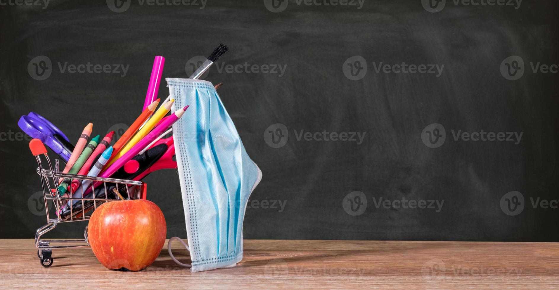Back to school concept with pencils, crayons in shopping cart with apple with face mask photo