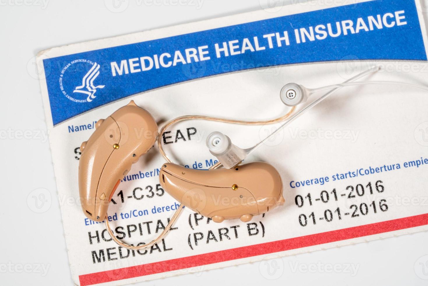 Close up of a pair of tiny modern hearing aids on medicare card background photo