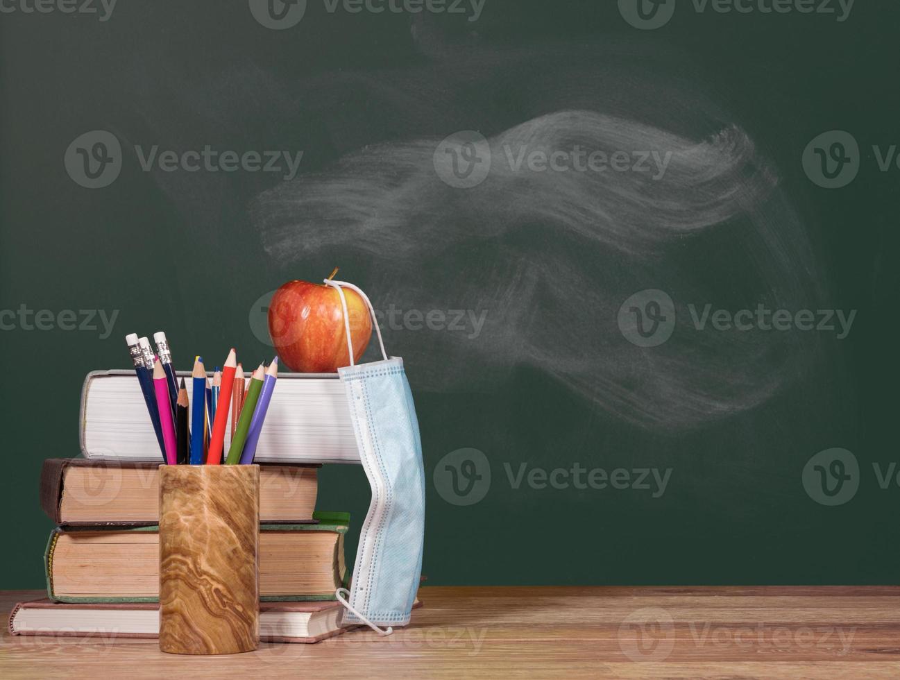 Back to virtual school background concept with stack of books and apple with face mask photo