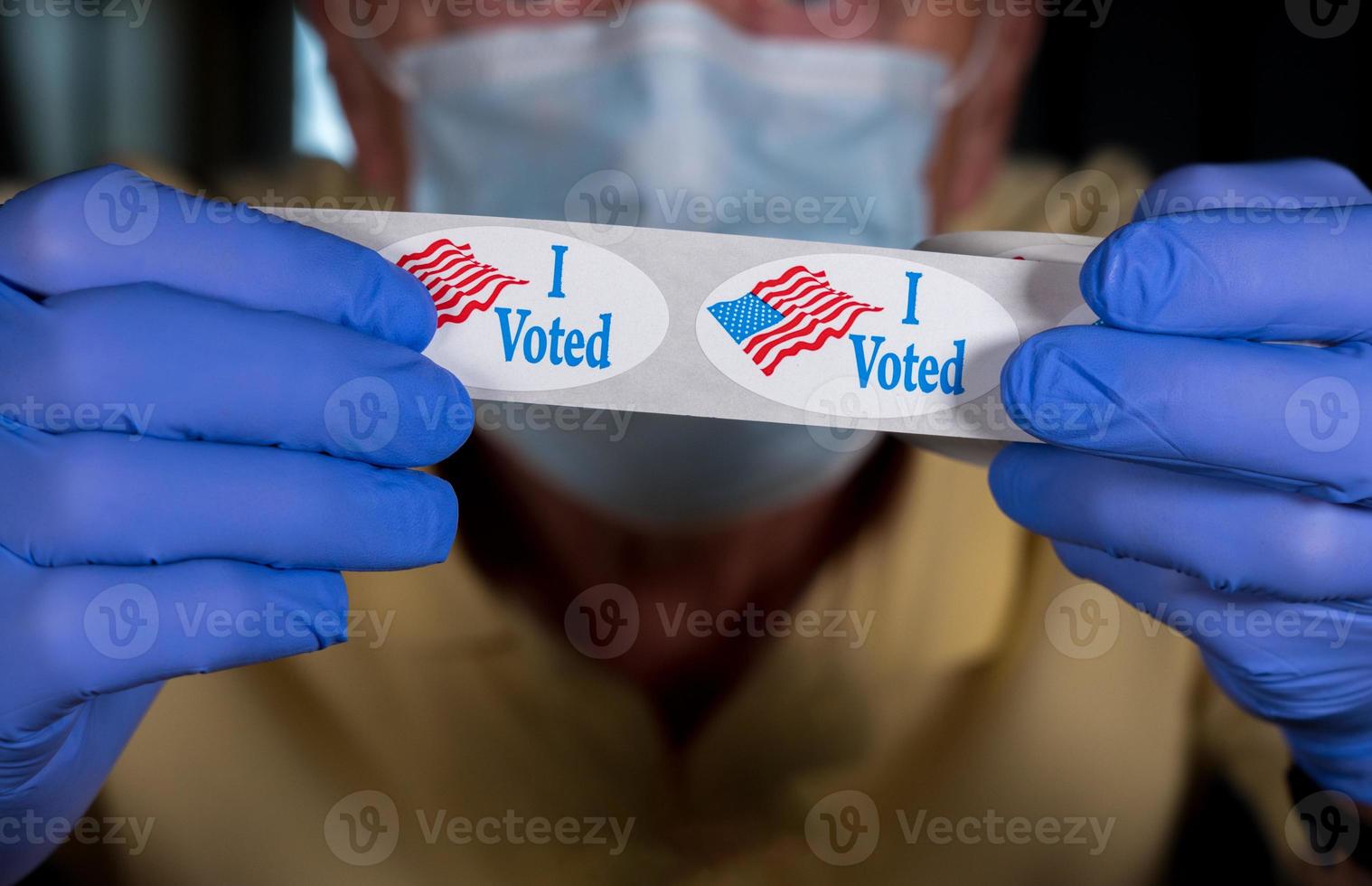 Gloved hands holding roll of I Voted stickers or buttons with USA flag ready for voter who voted in person in election photo