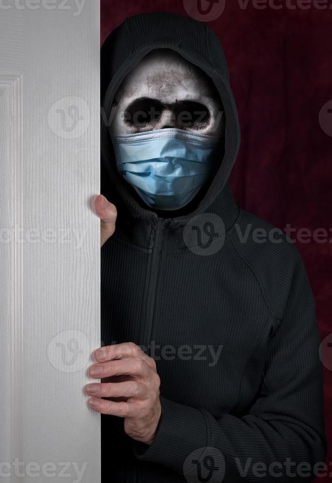 Halloween theme of stalker with skull and face mask against coronavirus entering a home photo