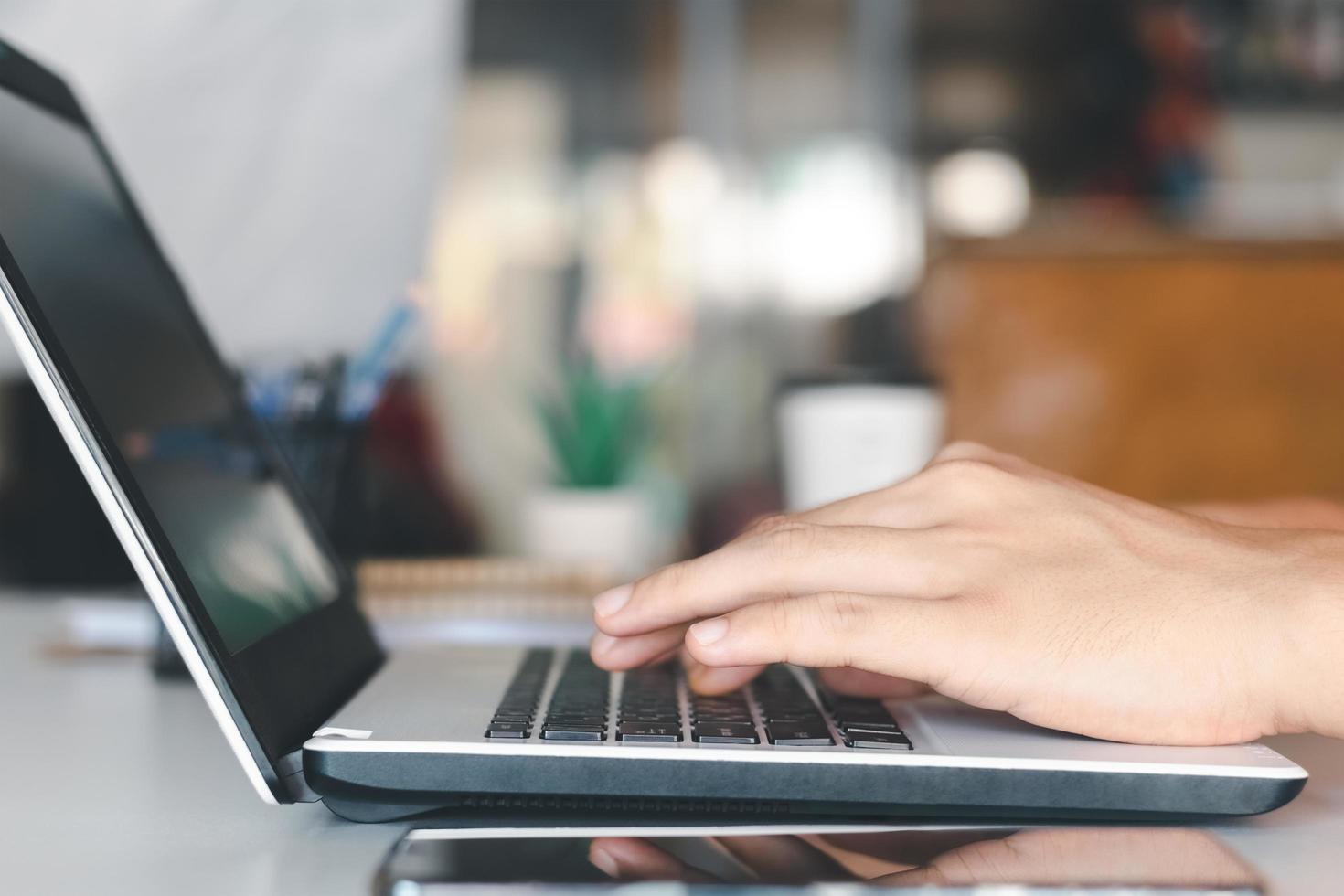 young man using laptop computer and mobile phone When looking for financial information in business, work at the desk. Writing with a pen, studying remotely from home and working from home. photo