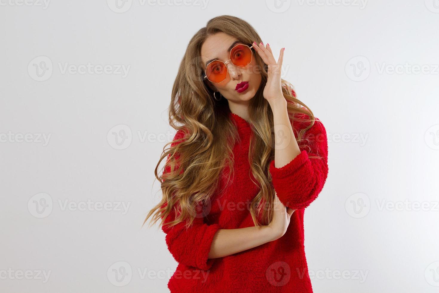 cara de mujer de primer plano con gafas de sol rojas aisladas en fondo blanco. chica con sudadera con capucha roja y maquillaje de labios rojos. concepto de belleza de moda. hermoso concepto de cabello y accesorios de moda. foto