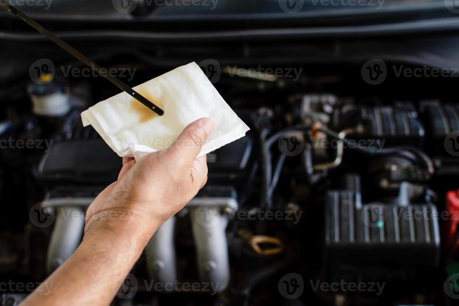 Concept of engine maintenance. A technician is checking the level of the engine oil. Man holding white tissue paper to wipe the engine oil. Close up, Blurred background photo