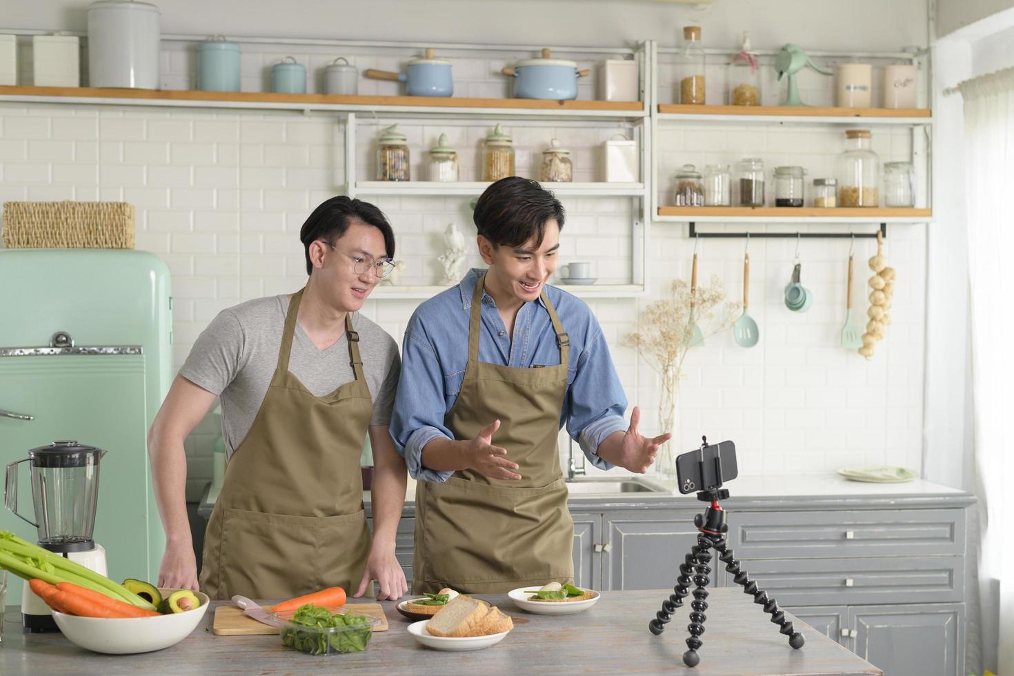 Young two close friend bloggers preparing food in the kitchen while live streaming via smartphone. photo