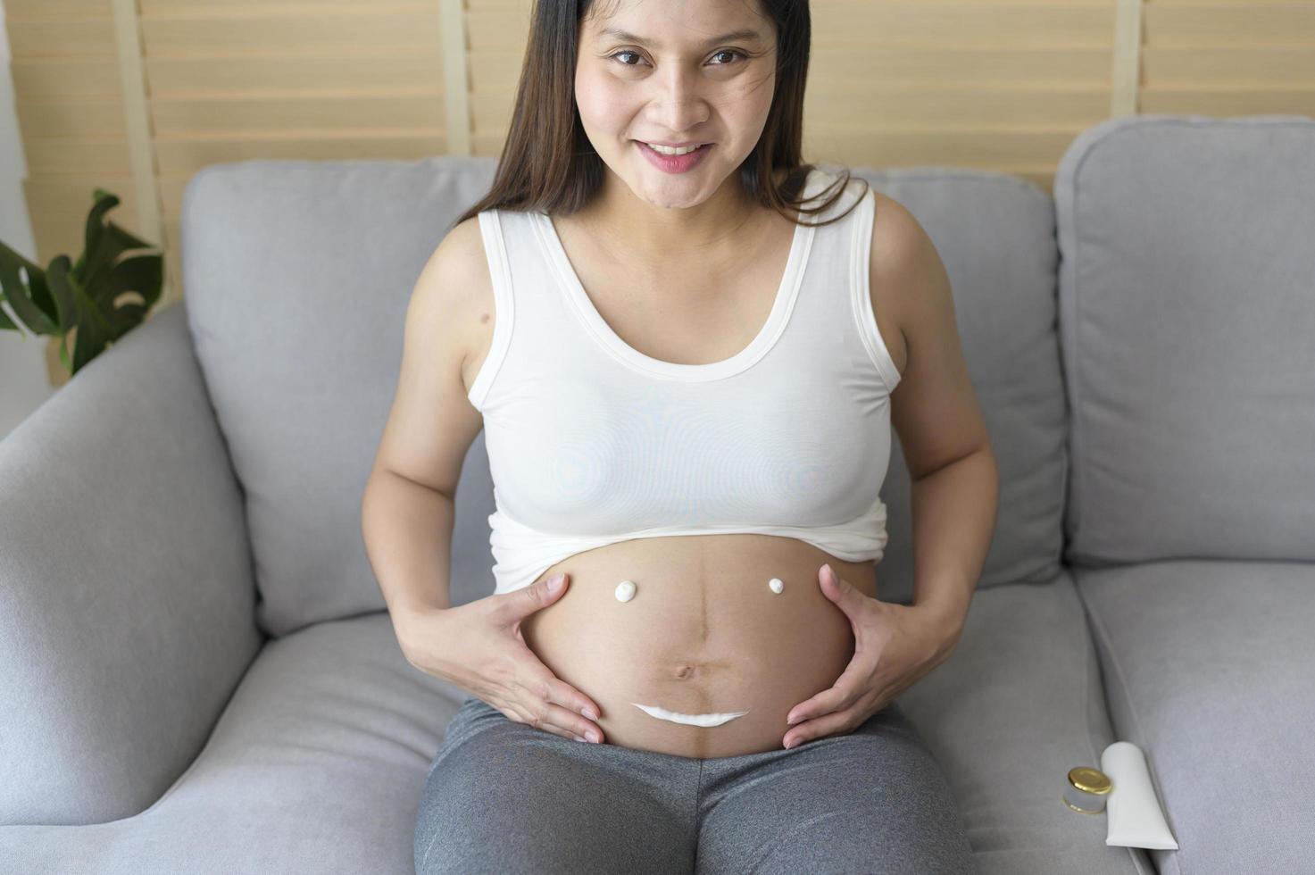 mujer embarazada joven que aplica crema hidratante en la barriga, atención médica y atención del embarazo foto