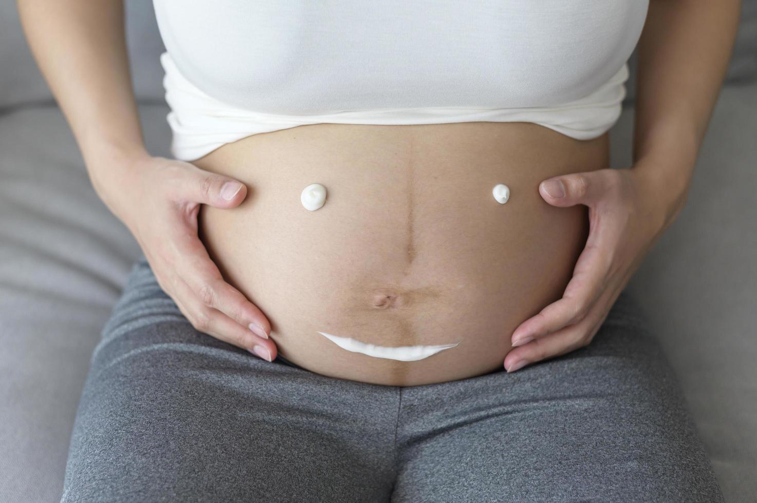 mujer embarazada joven que aplica crema hidratante en la barriga, atención médica y atención del embarazo foto