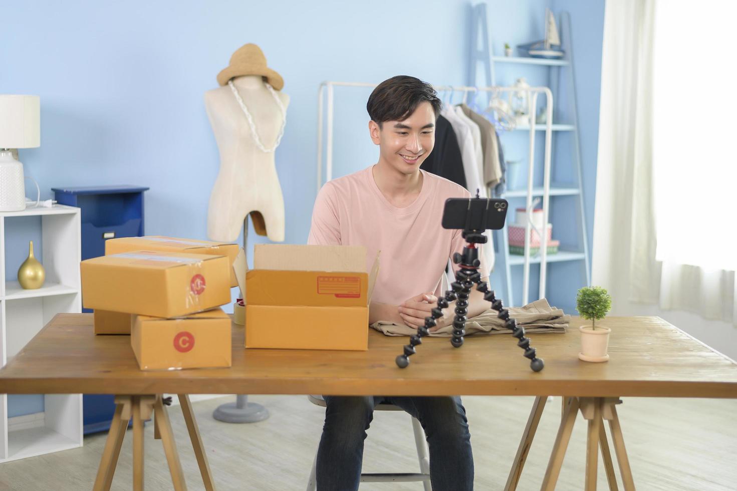 An Asian man is showing clothes in front of smartphone  live streaming at his shop. Technology online business concept. photo