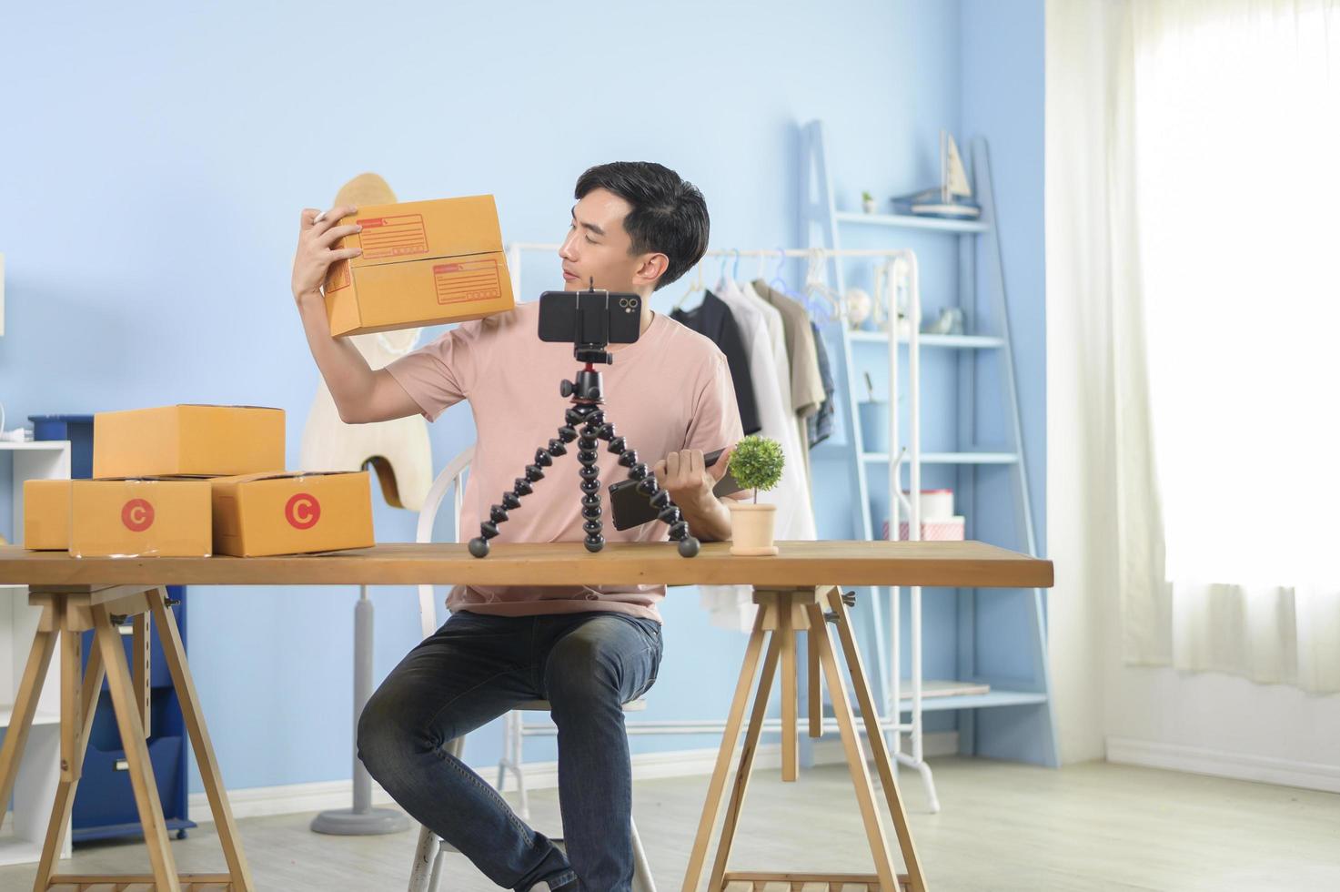 An Asian man is showing clothes in front of smartphone  live streaming at his shop. Technology online business concept. photo