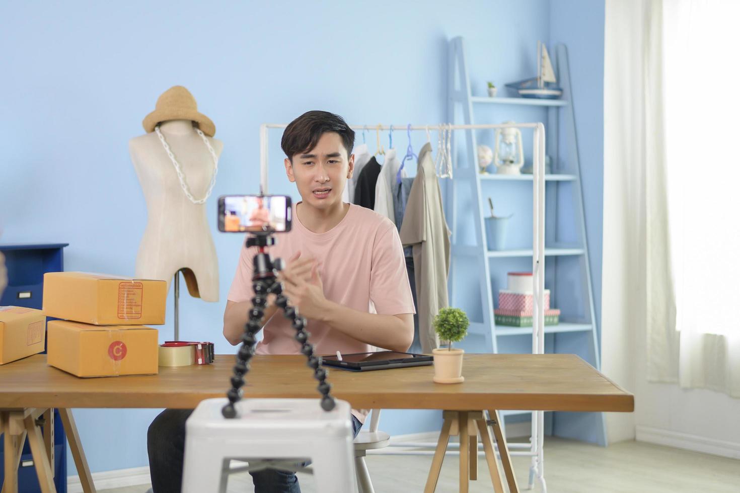 An Asian man is showing clothes in front of smartphone  live streaming at his shop. Technology online business concept. photo