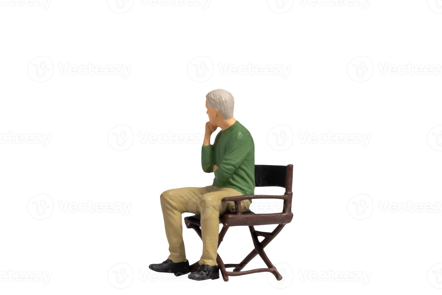 Miniature people sitting on chair isolated on white background photo