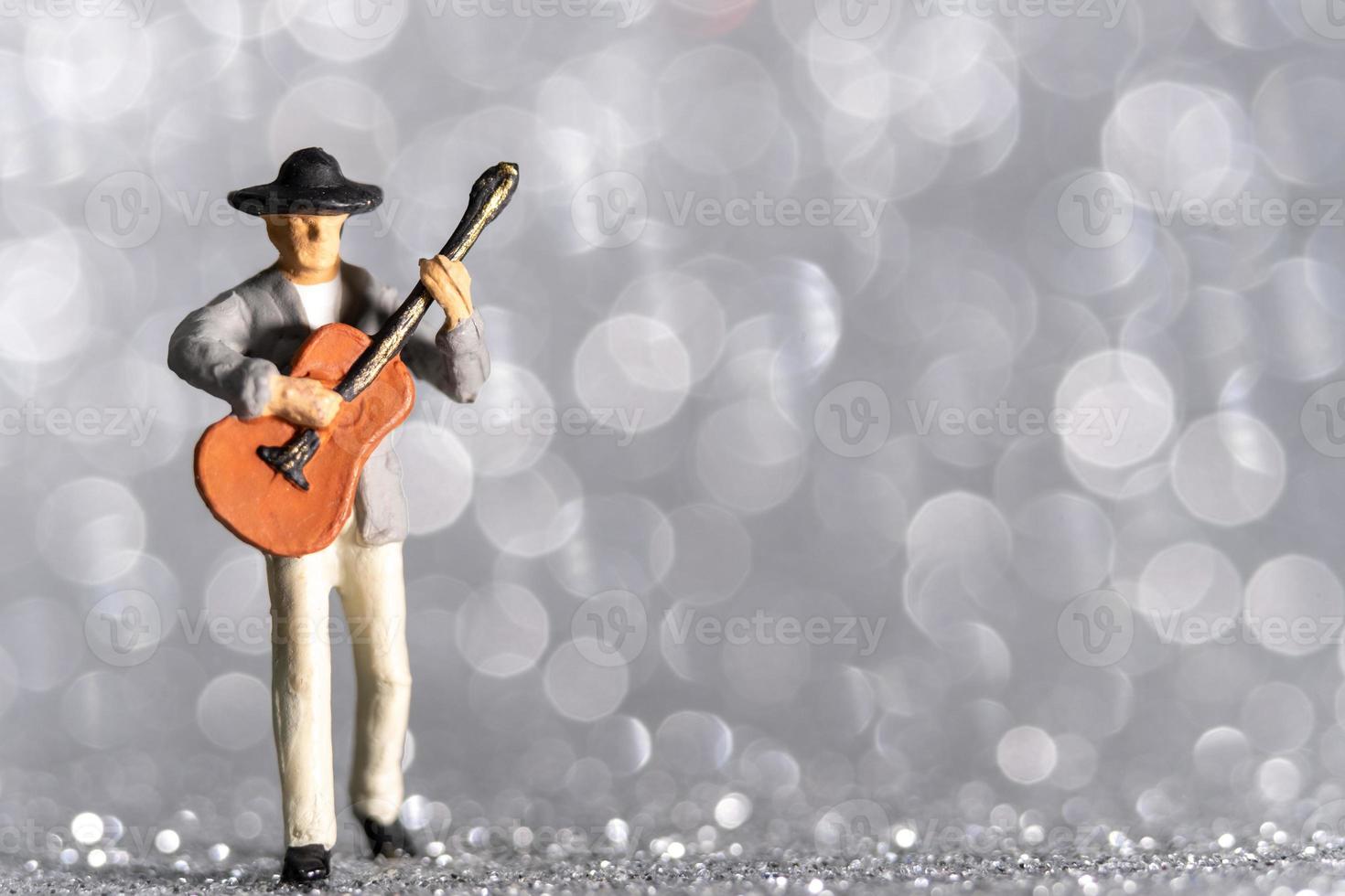 Músico en miniatura con guitarra sobre fondo bokeh foto