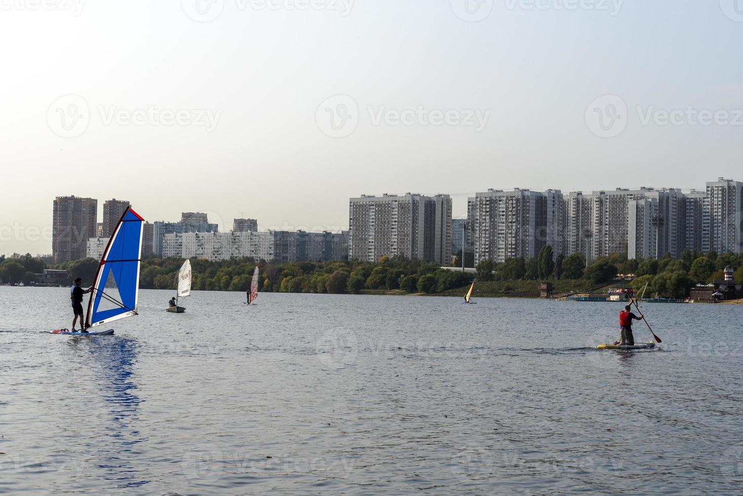 Windsurfer. Man is surfing on the background of skyscrapers. Man on a windsurf board. Windsurfing in the city. Water sports. Surfing with a sail. Windsurfing equipment. Active lifestyle. photo