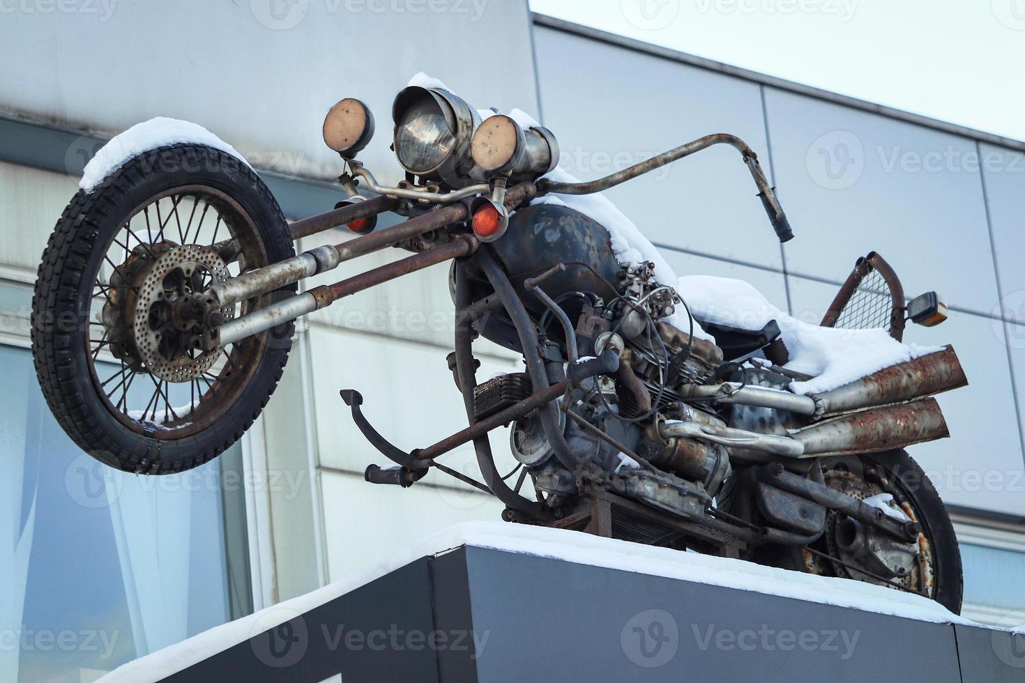 Old motorcycle standing as a sign on roof in winter snow photo