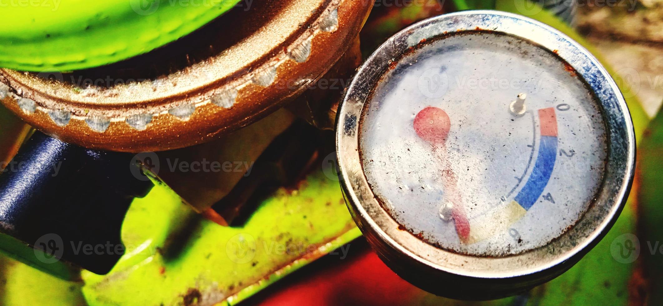 An old and dull gas meter on the green gas cylinder under the dim light background photo