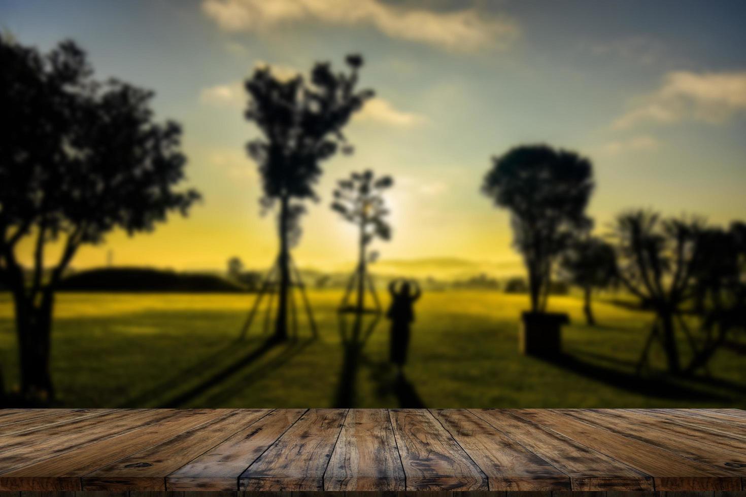 mesa de madera y desenfoque de belleza en un día de puesta de sol en un campo con cielo y montañas en el fondo. foto