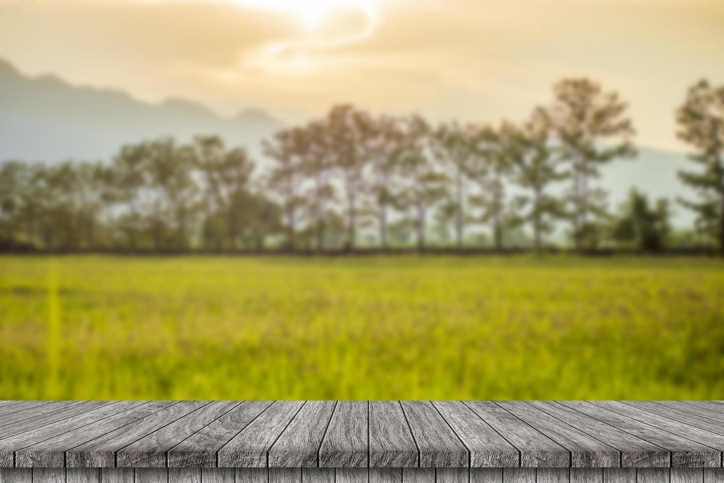 mesa de madera y desenfoque de belleza en un día de puesta de sol en un campo con cielo y montañas en el fondo. foto