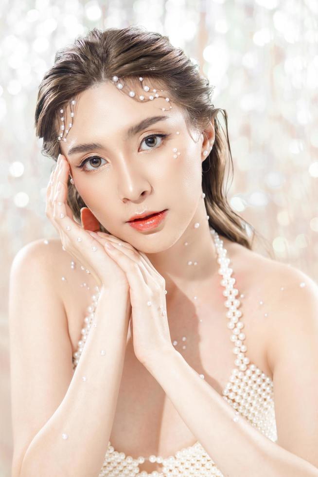 Beautiful young asian woman with clean fresh skin with pearls on glitter background. Face care, Facial treatment, beauty and spa, Cute Asian women portrait. photo