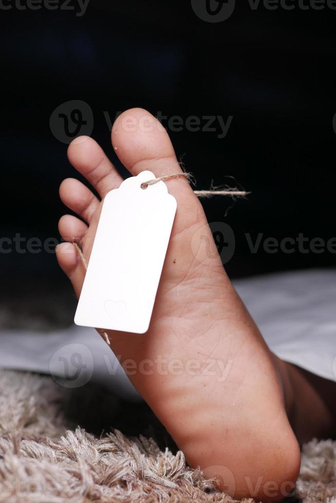 The dead man's body with blank tag on feet under white cloth in a morgue photo