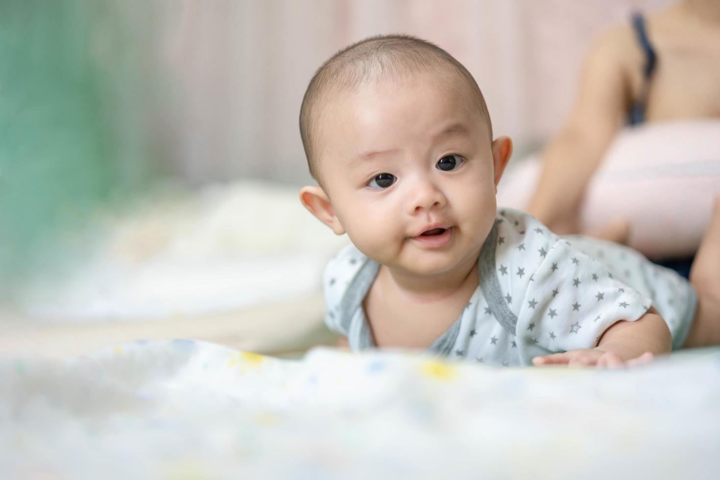 Happy family, Cute Asian newborn baby lying play on bed looking at something. While your mother takes care with love nearby. Innocent little boy on the first day of his life. Mother's Day concept. photo