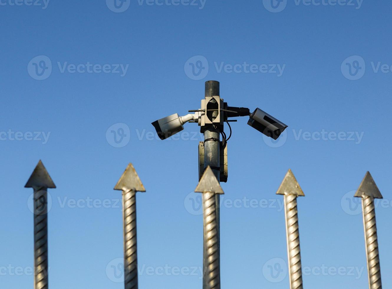 Two video cameras over iron fence spikes on blue sky photo