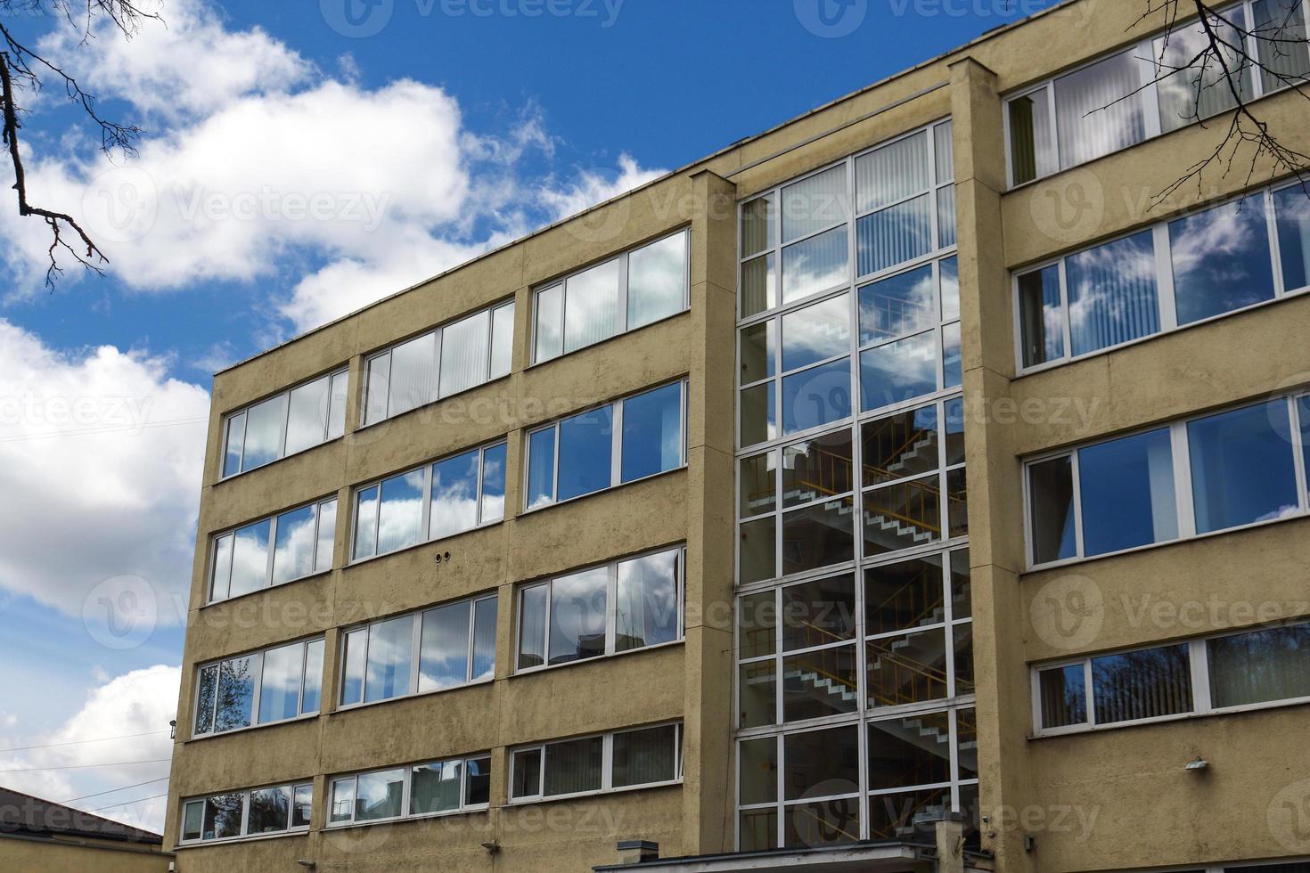 Sky and clouds reflected in yellow concrete building windows with visible staircase photo