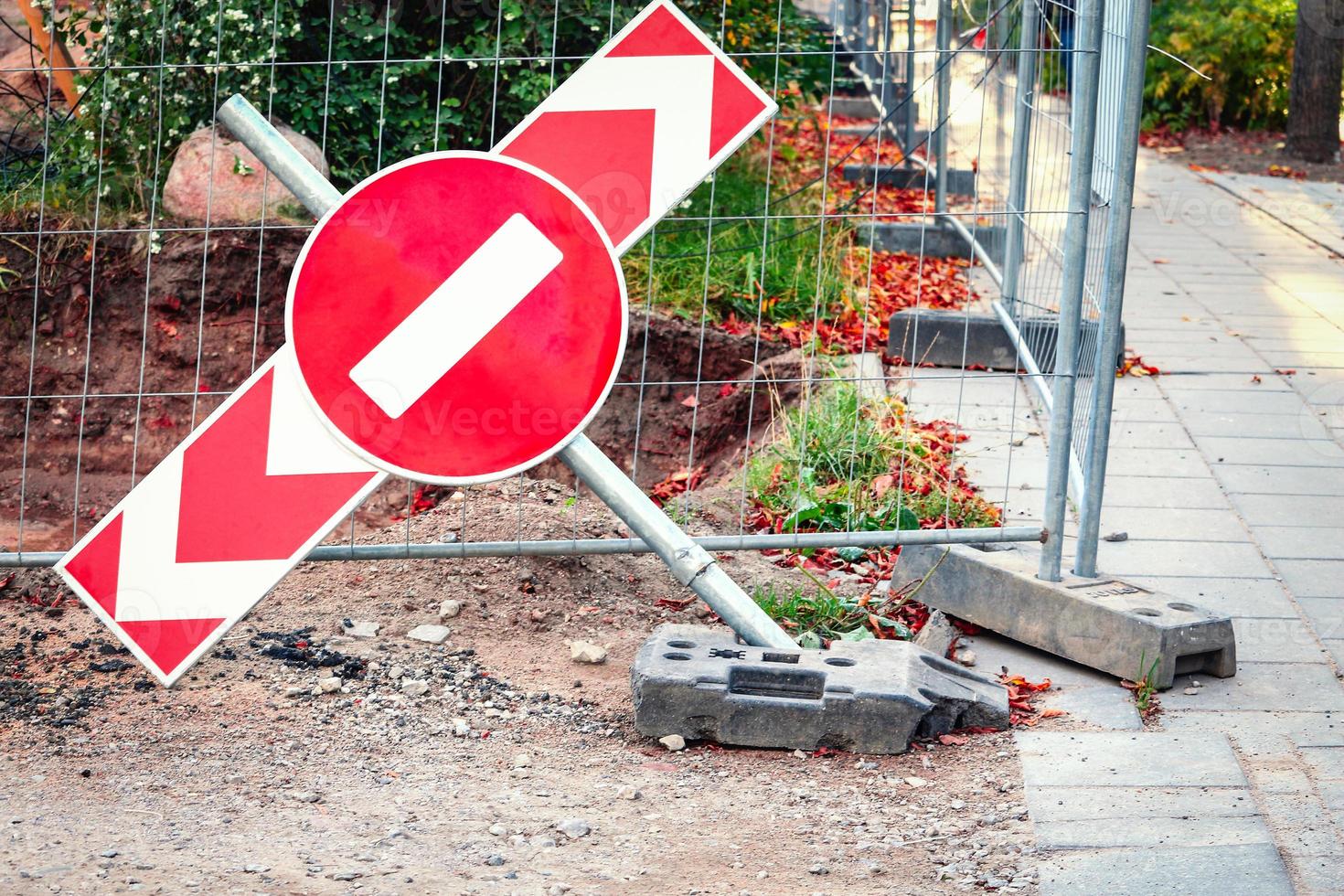 Red stop road sign on red arrow sign falling on ground near construction site and road photo