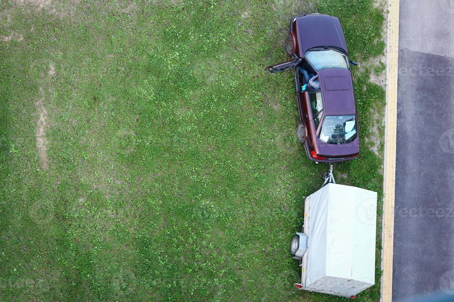 Top down view on car with man sitting inside and trailer standing near road photo