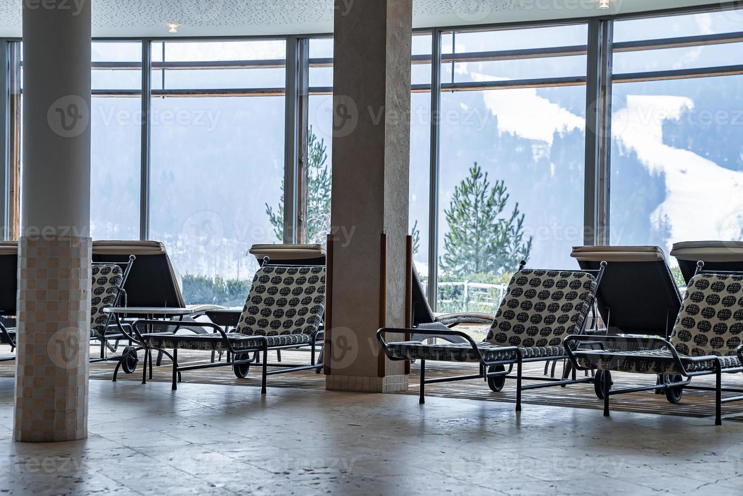 Empty chaise lounge chairs arranged in lobby with view of snowy mountains photo