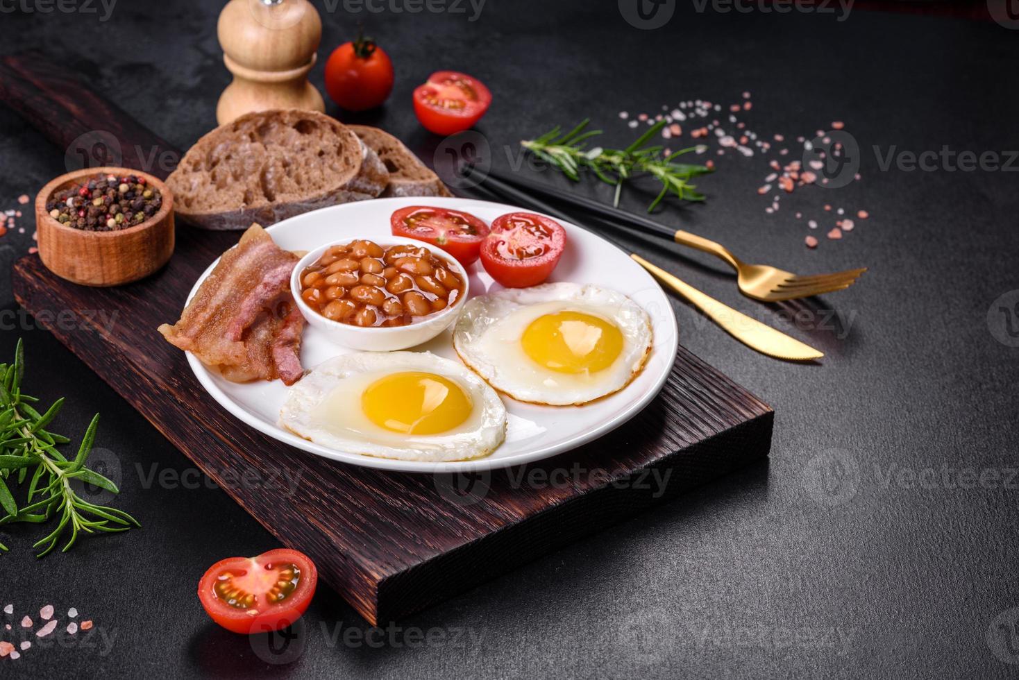 English breakfast with fried eggs, bacon, beans, tomatoes, spices and herbs photo