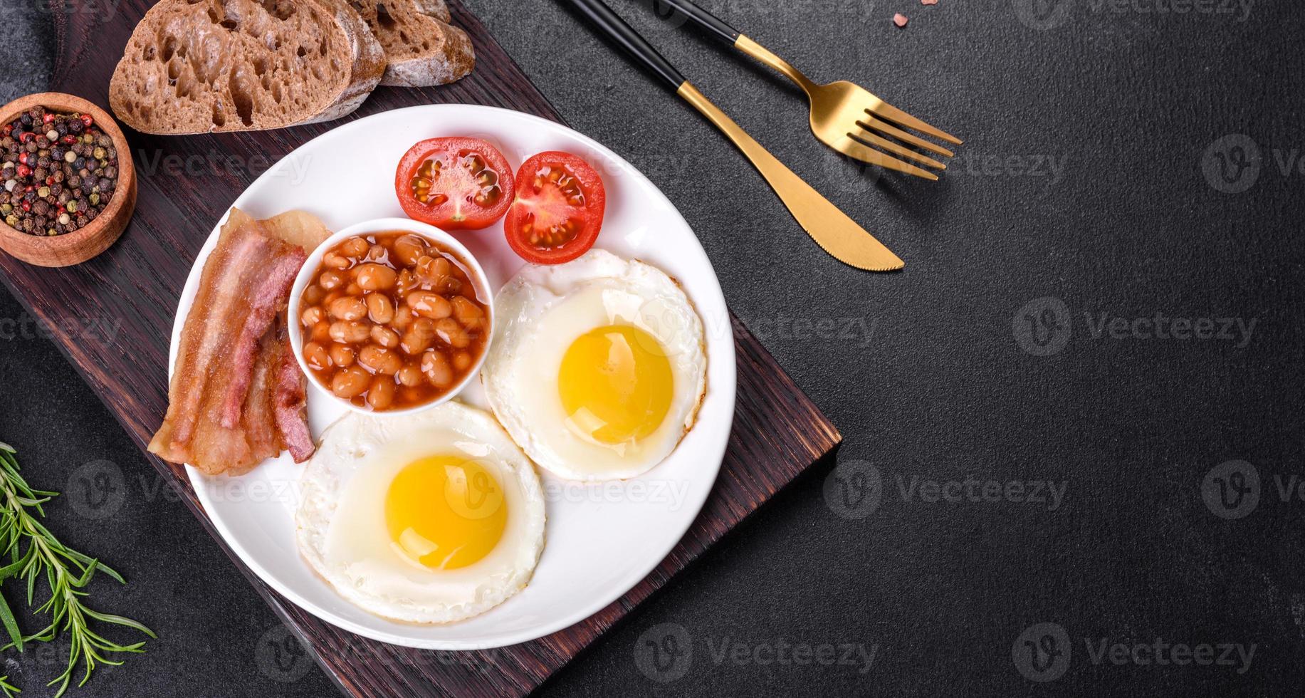 English breakfast with fried eggs, bacon, beans, tomatoes, spices and herbs photo