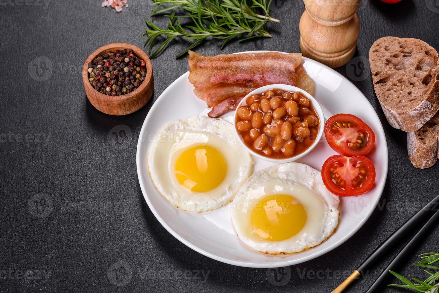 English breakfast with fried eggs, bacon, beans, tomatoes, spices and herbs photo