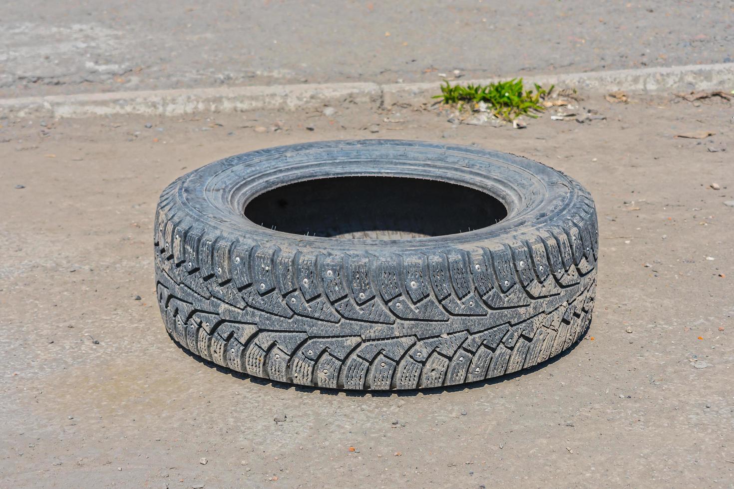 Thrown out on a deserted road, an old, worn-out winter tire from a car wheel photo