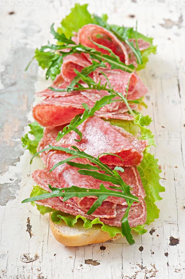 Sandwich with salami, lettuce, tomato and arugula photo