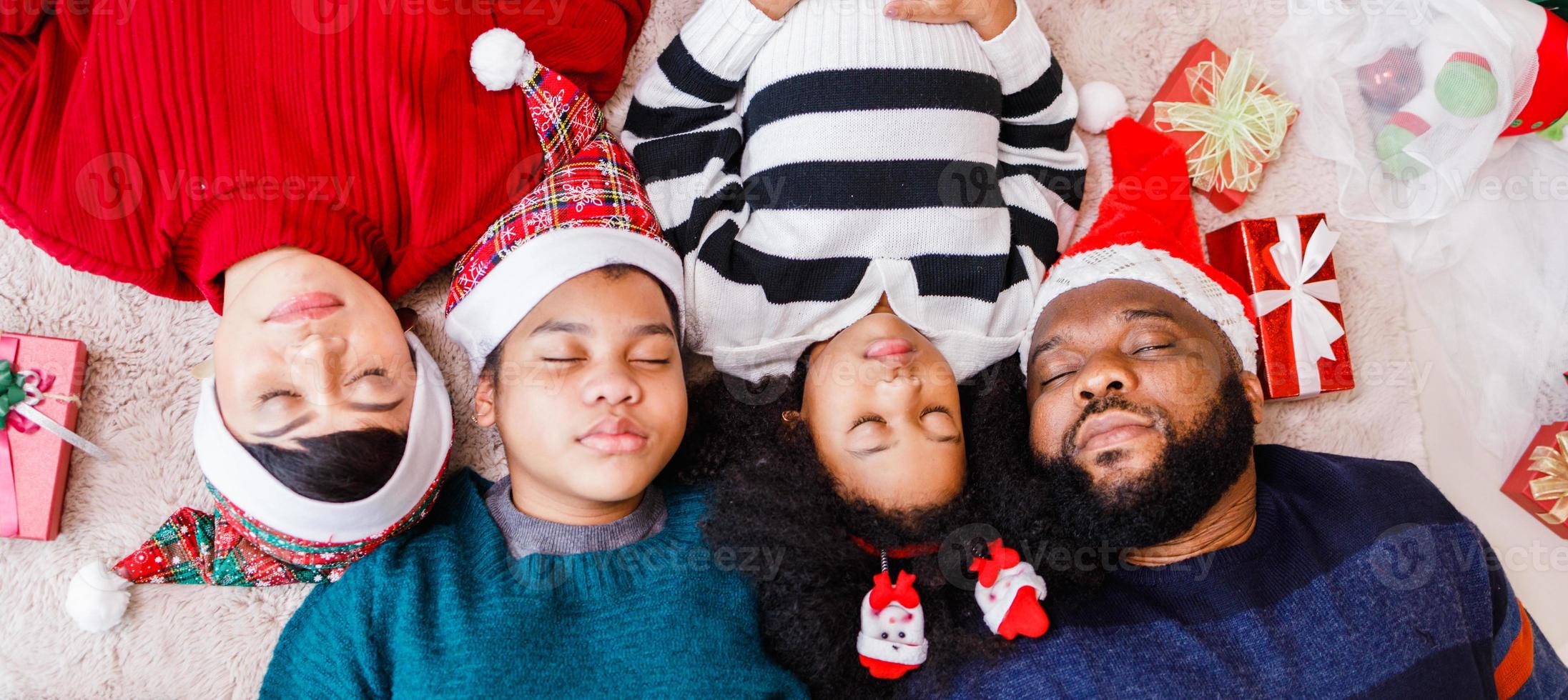 familia afroamericana en tema navideño. feliz familia afroamericana de cuatro personas que se unen en el suelo juntos. foto