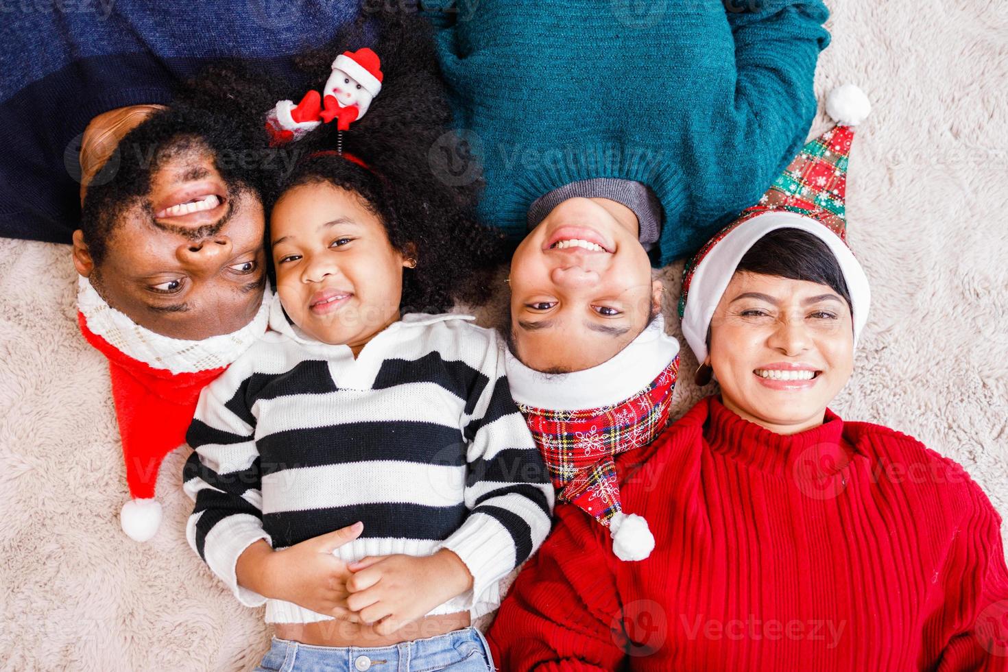 familia afroamericana en tema navideño. feliz familia afroamericana de cuatro personas que se unen en el suelo juntos. foto