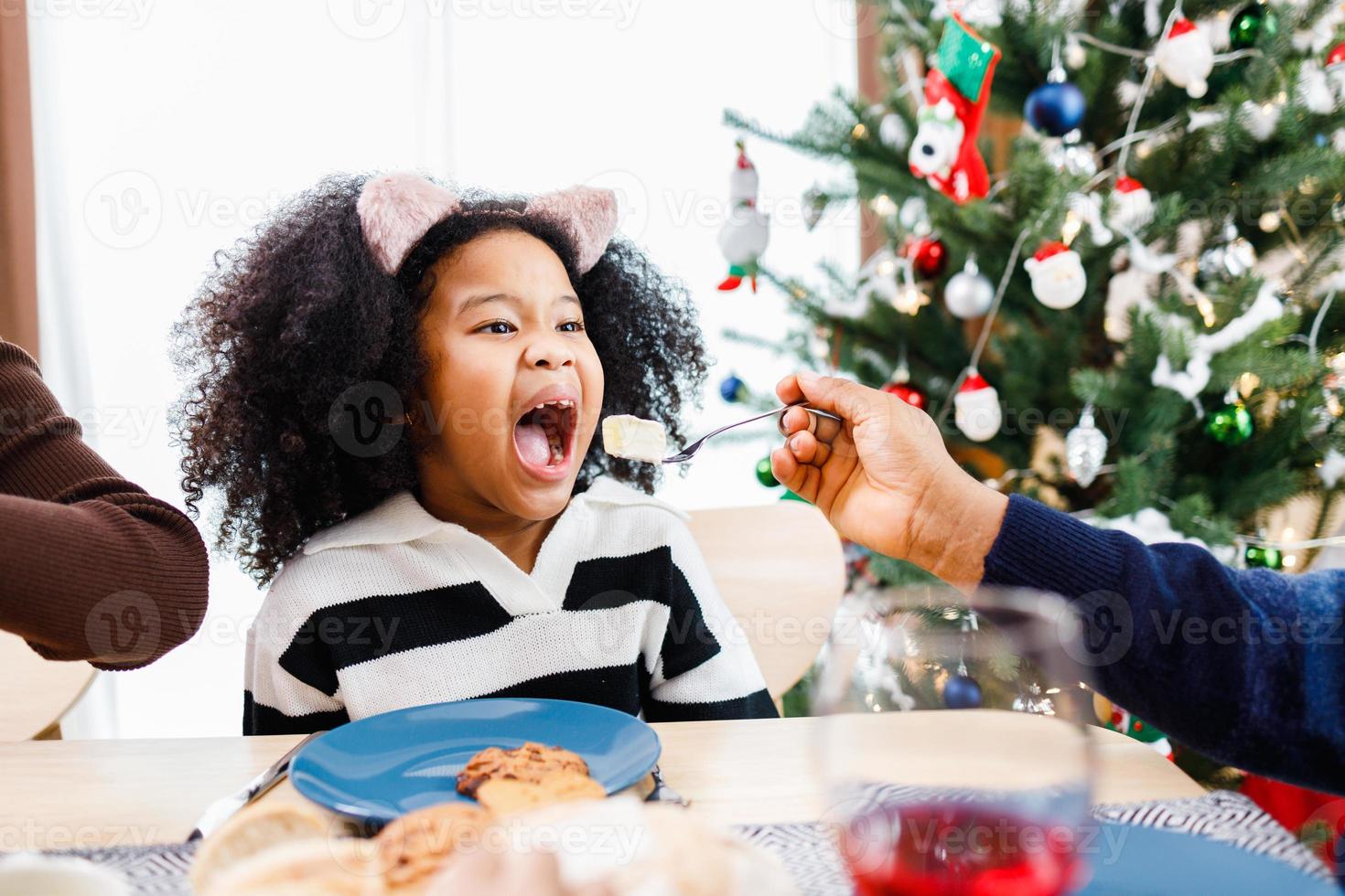 la familia feliz está cenando en casa. celebración de vacaciones y unión cerca del árbol de navidad. familia afroamericana. foto