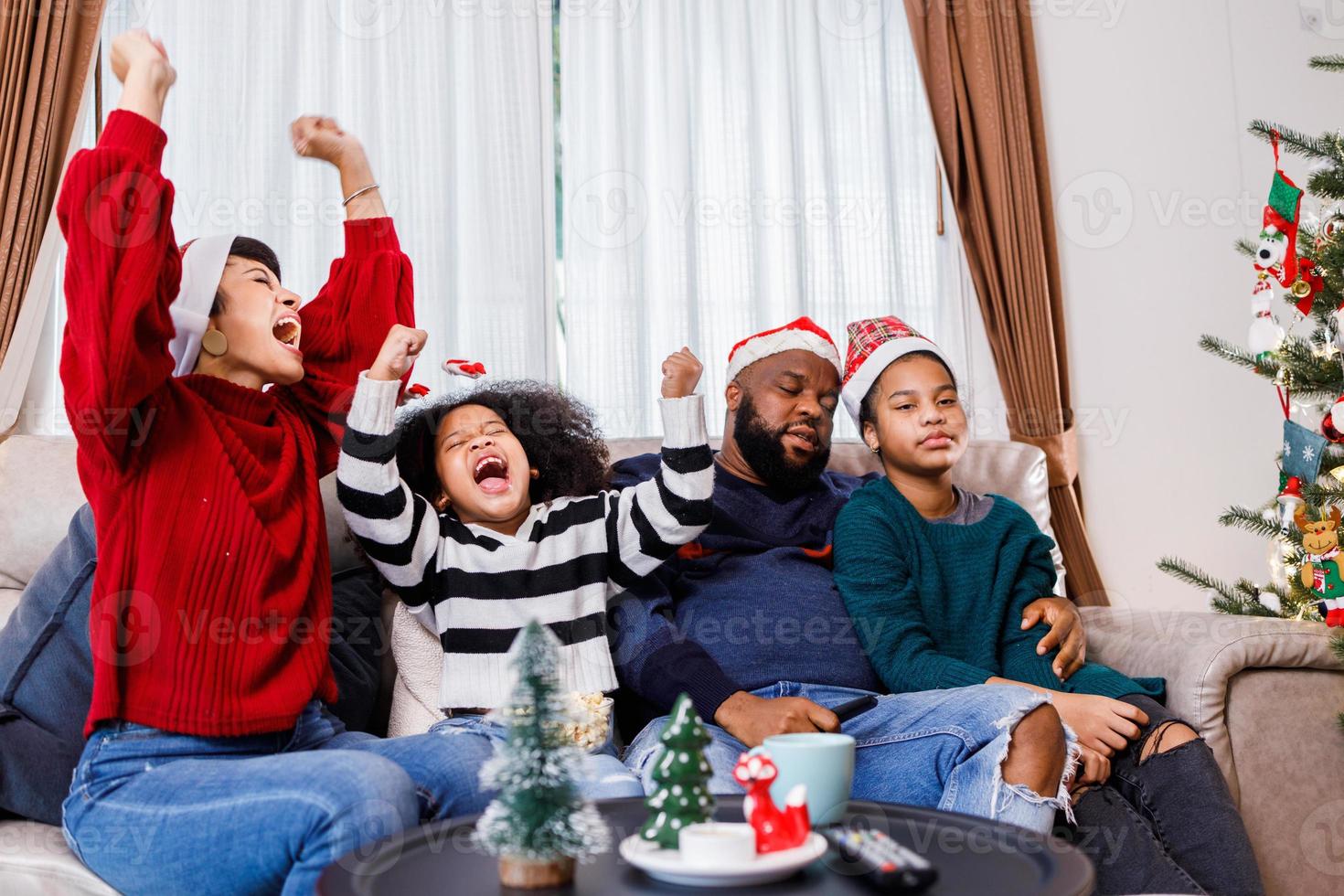 familia afroamericana en tema navideño. la familia feliz se divierte sentada en el sofá de casa. foto