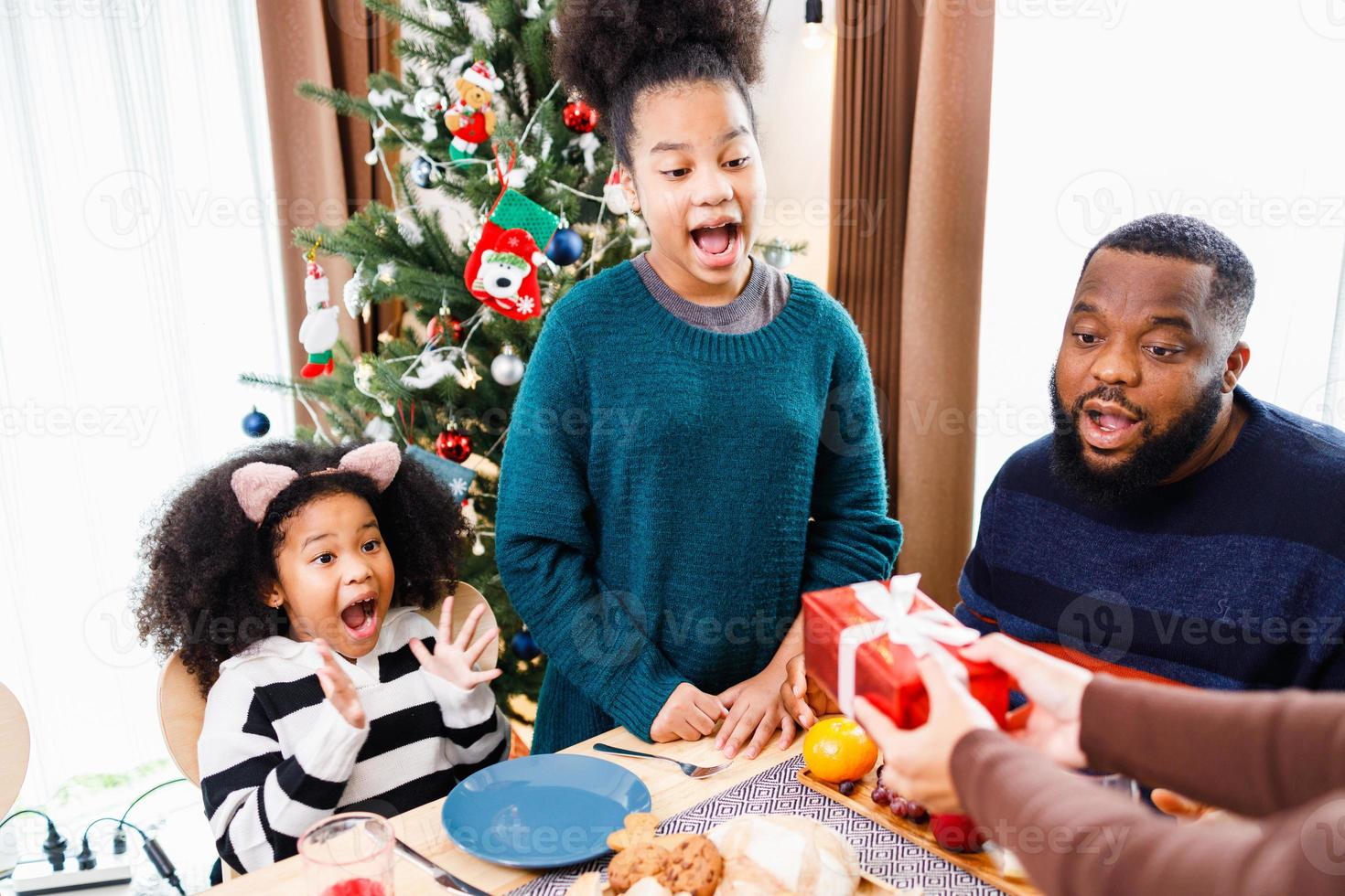 familia afroamericana sorprendiendo junto con un regalo el día de navidad durante la cena. foto