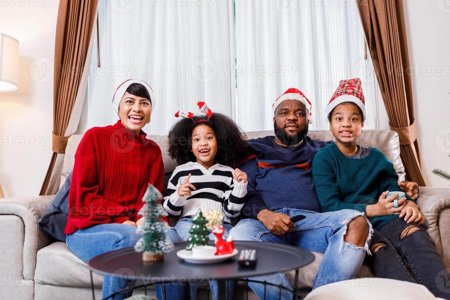 familia afroamericana en tema navideño. la familia feliz se divierte sentada en el sofá de casa. foto