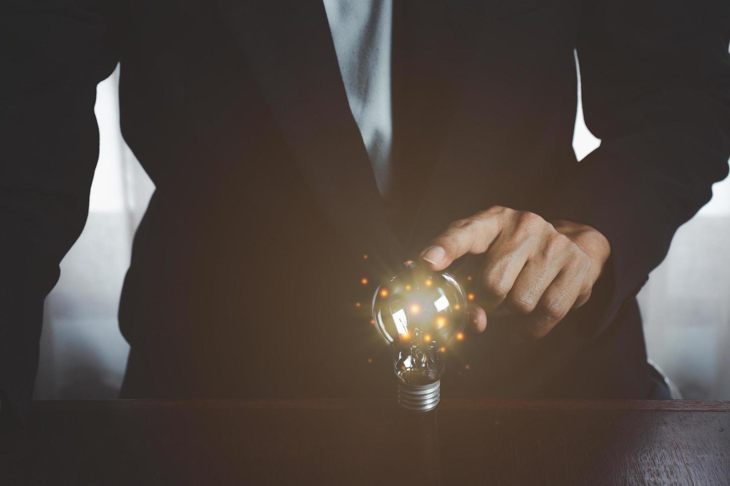 hombre de negocios tocando una bombilla de luz brillante. concepto de ideas para presentar nuevas ideas gran inspiración e innovación nuevo comienzo. foto