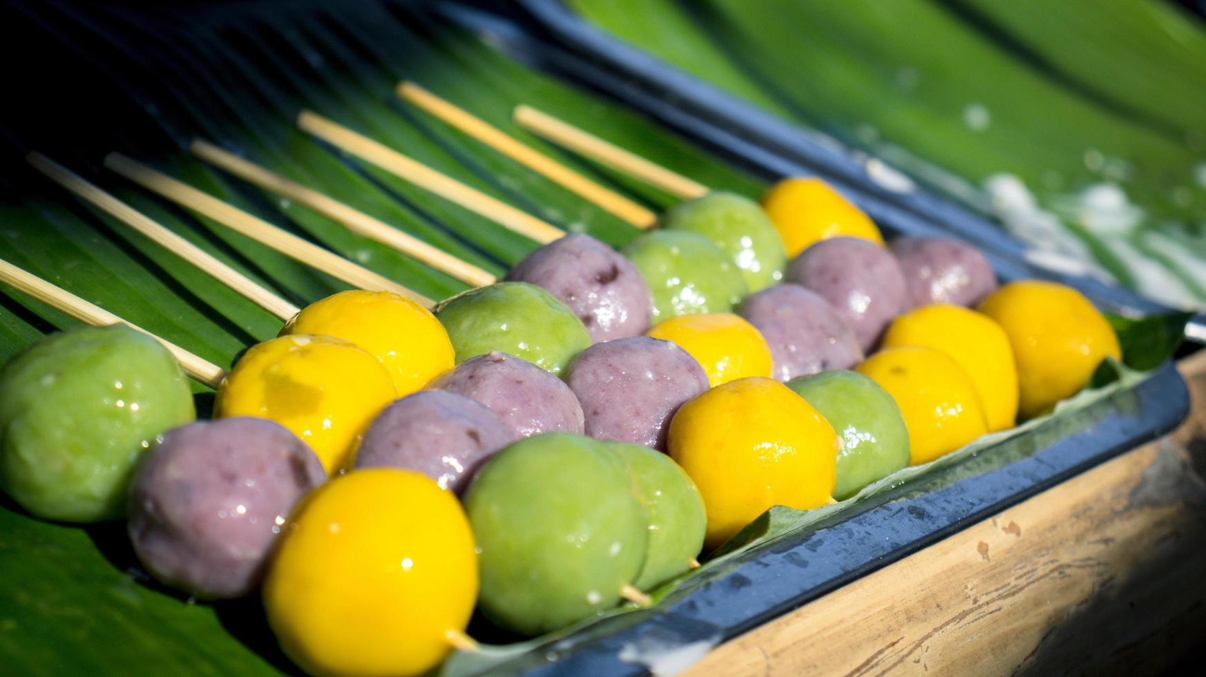 Sweets made from green, purple, yellow flour, skewers placed on green banana leaves. photo