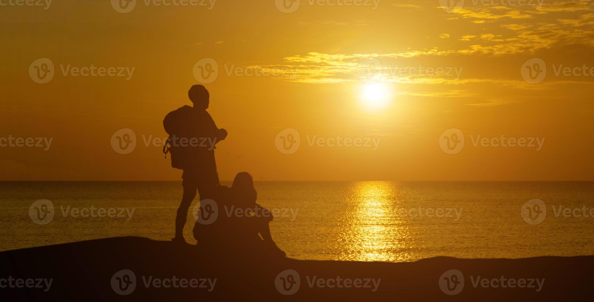 A panoramic view of the silhouette of men and women looking at the serene sunset . photo