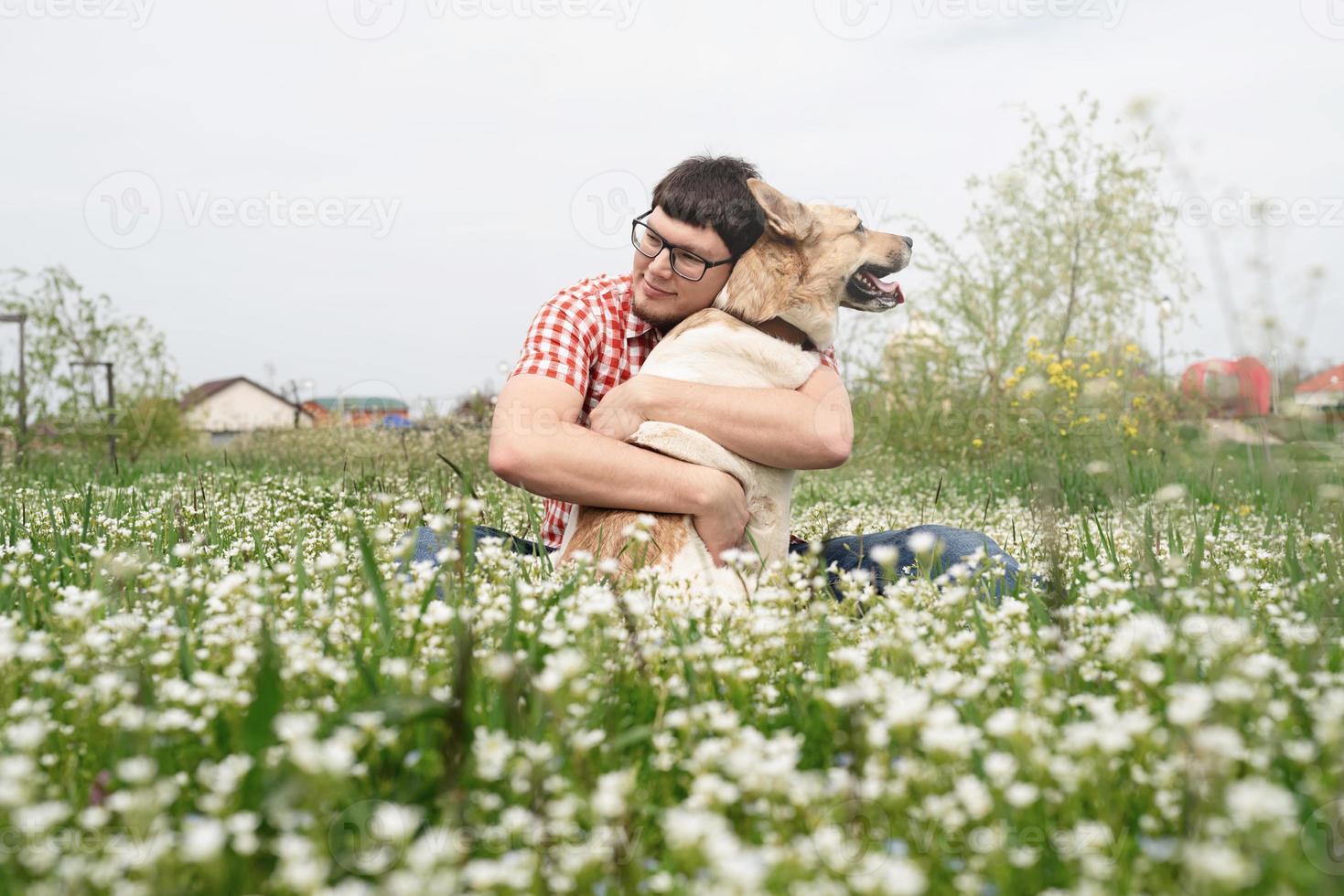 hombre feliz sentado con un perro pastor de raza mixta sobre hierba verde en flores de primavera foto