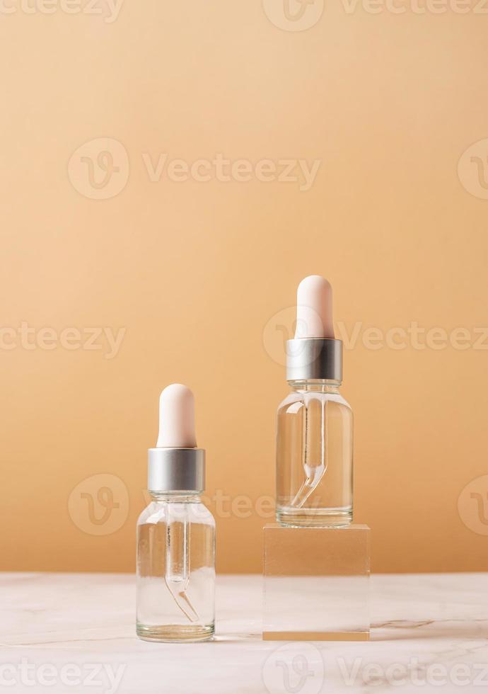 Glass dropper bottles with a pippette with black rubber tip on glass podium and beige background, mockup design photo