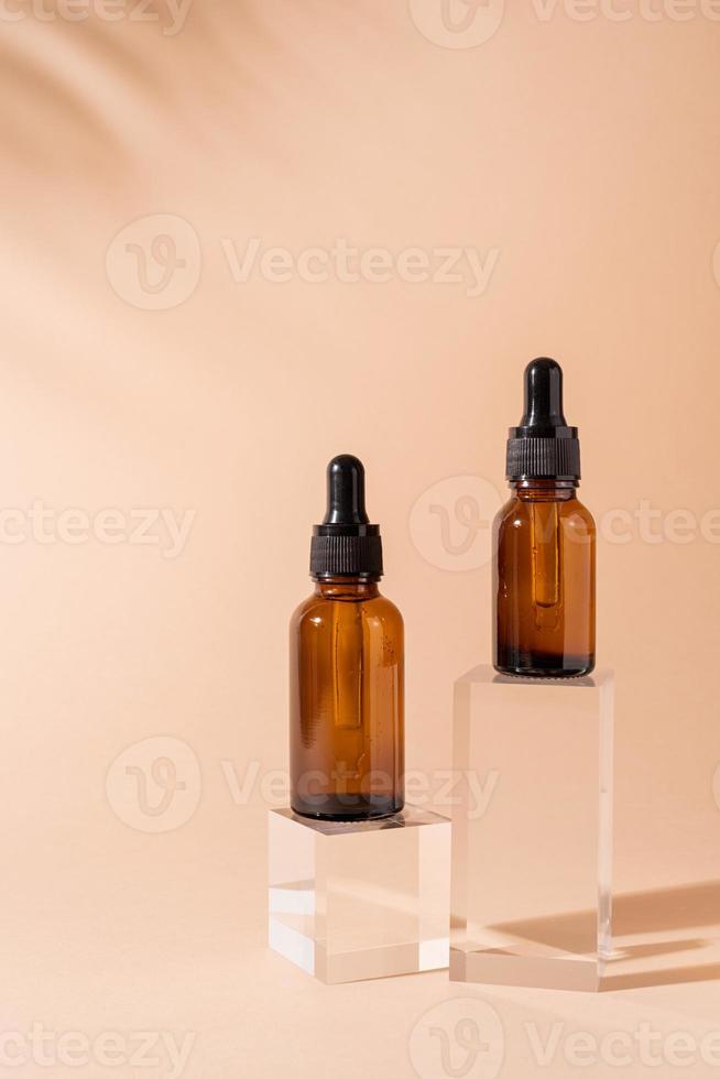 frascos cuentagotas de vidrio con una pipeta con punta de goma negra sobre podio de vidrio y fondo beige, diseño de maqueta foto
