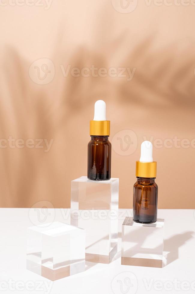 Amber glass dropper bottles with a pippette with white rubber tip on glass podium and beige background, mockup design photo