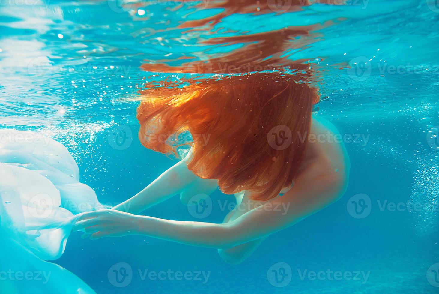 retrato de una joven sonriente y hermosa chica pelirroja en un día soleado en una piscina abierta en verano bajo el agua foto