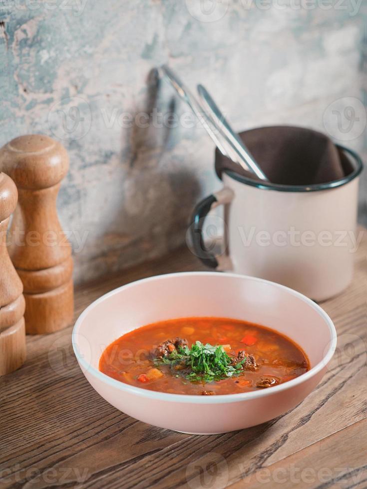 goulash rojo en el plato, sal, pimienta, cubiertos y vino tinto caliente en la mesa foto